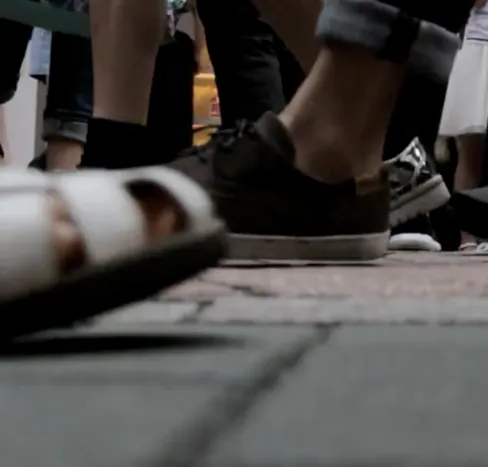 石畳を歩く人々の足元のクローズアップで手前の白いサンダルと中央の茶色いレザーシューズが街を往来する賑やかな雰囲気